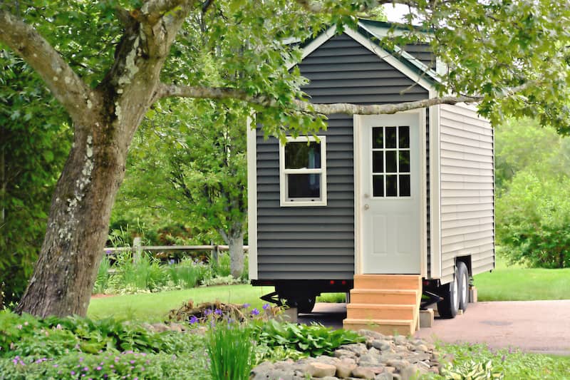 Gray tiny house on wheels on a sunny day.