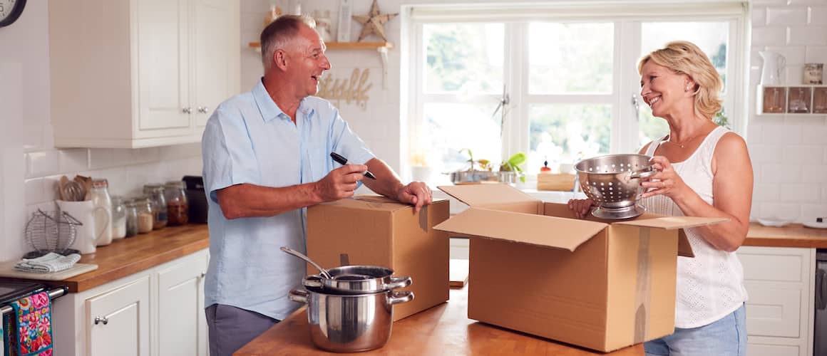 A senior couple packing and labeling boxes in a kitchen, signifying moving or packing activities for relocation.
