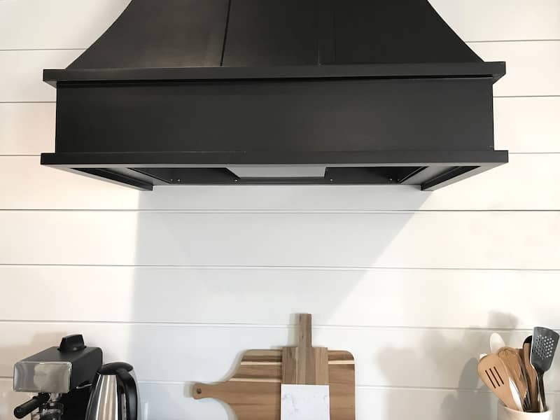 Painted white wood shiplap backsplash contrasted with black range hood over stovetop.