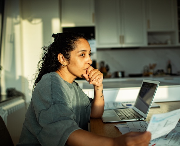Woman paying bills at kitchen table and working on laptop.