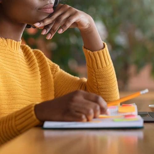 Woman wearing a yellow sweater with a journal and a pencil.