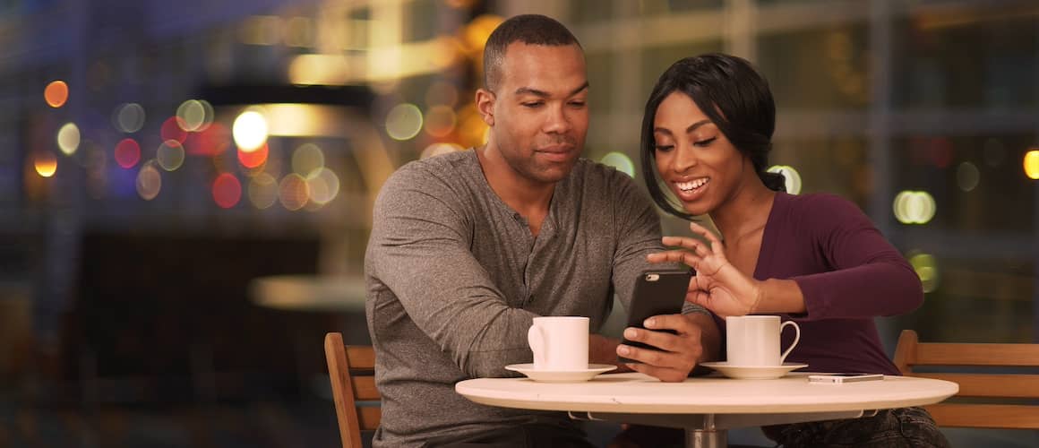 Young couple sitting at cafe table looking at cell phone.