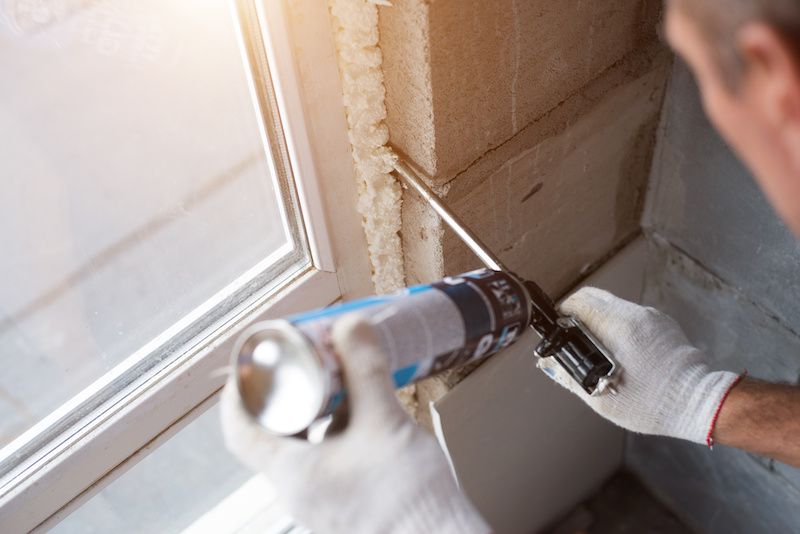 RHB Assets From IGX: Man caulking a window for energy efficiency.