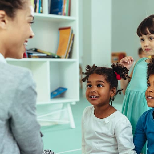A diverse group of children sitting attentively in a classroom, engaged in learning and interacting with their teacher and peers.
