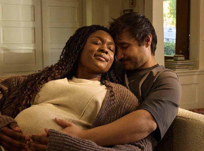 A couple sitting on a couch, with the pregnant woman resting and the man holding her belly supportively.