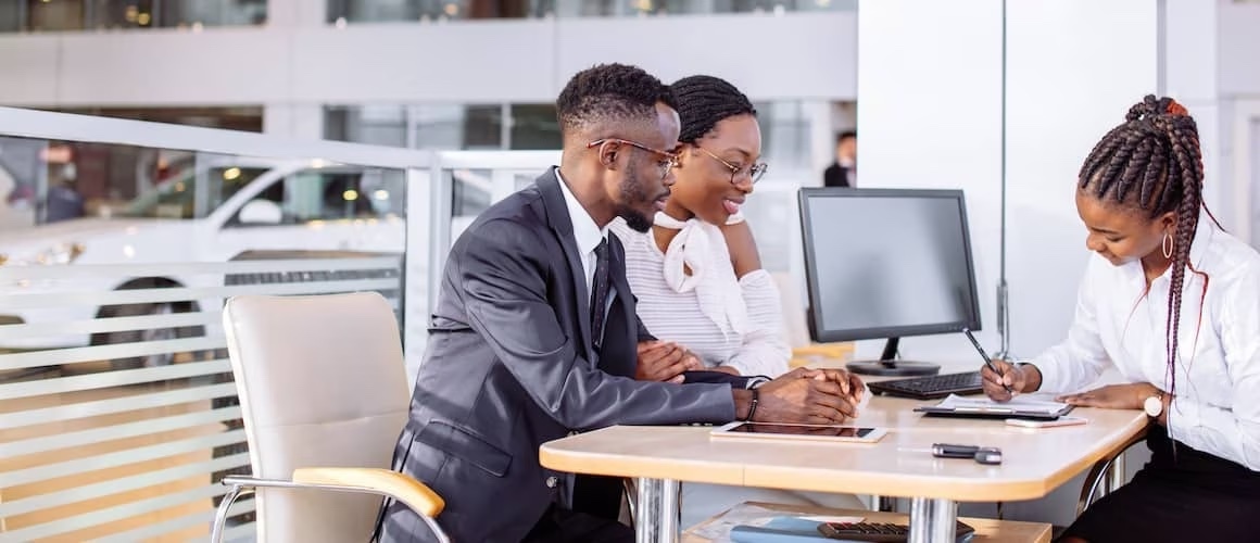 Couple sitting at car dealership with car salesperson.