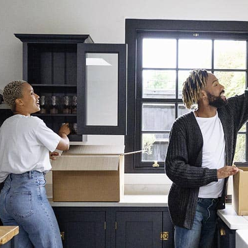 A young black couple moving into a new home, carrying boxes and belongings.
