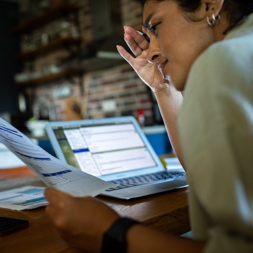 Woman reviewing bills on paper and online.