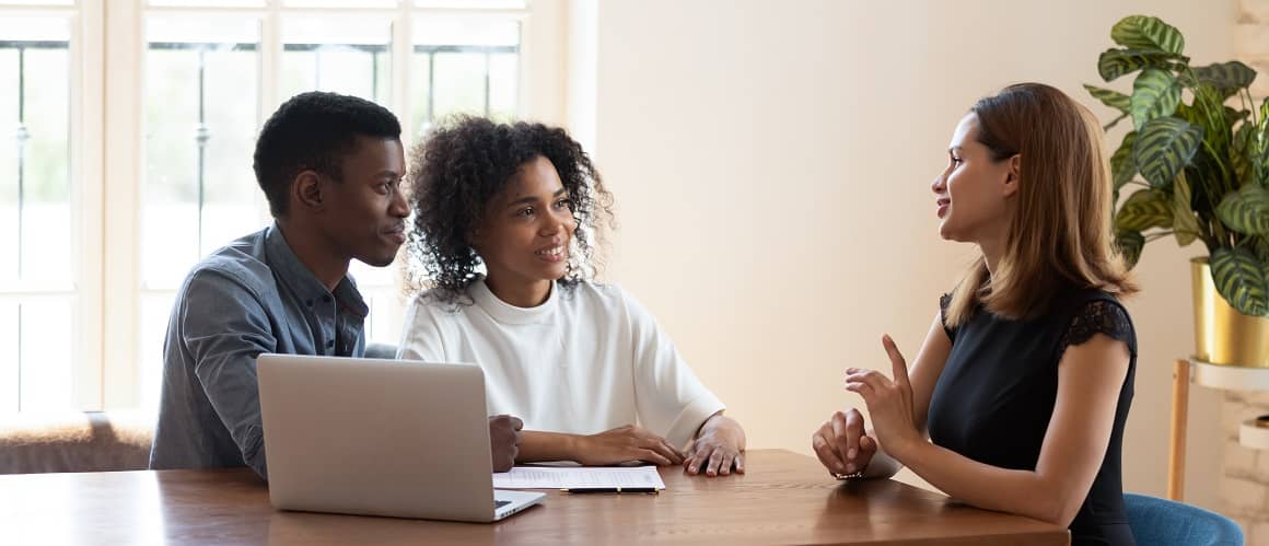 Young African American couple listening to lawyer at table with laptop.