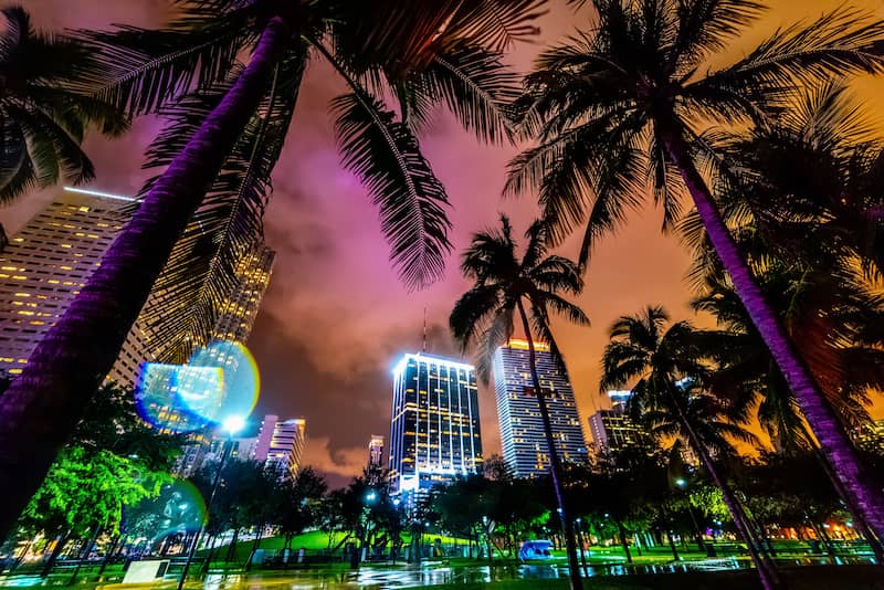 RHB Assets From IGX: Aerial view of Miami's skyline at night, illuminated by the city lights reflecting on the water.