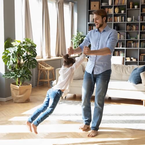 A father spins his daughter around by her hands in their living room.