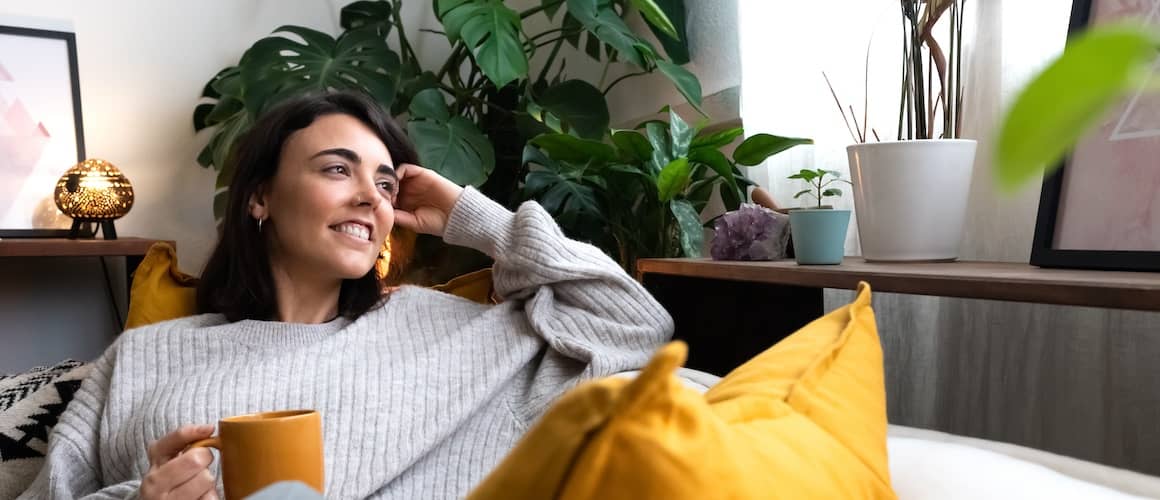 Happy young woman relaxing at home with tea looking out the window