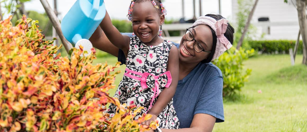 Afro American woman watering her flowers and plants with her daughter.