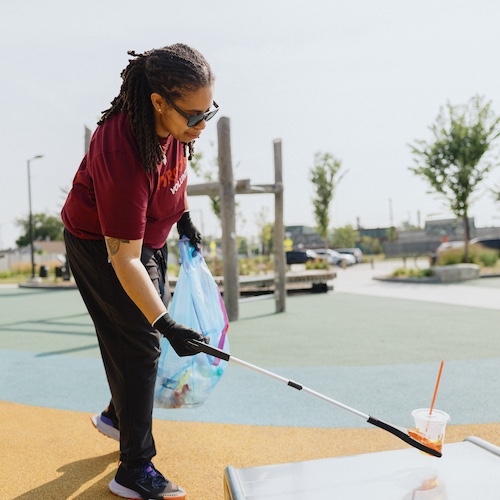 Rocket volunteer picking up plastic cup with metal claw in park.