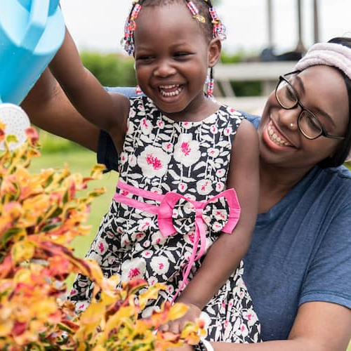 Afro American woman watering her flowers and plants with her daughter.