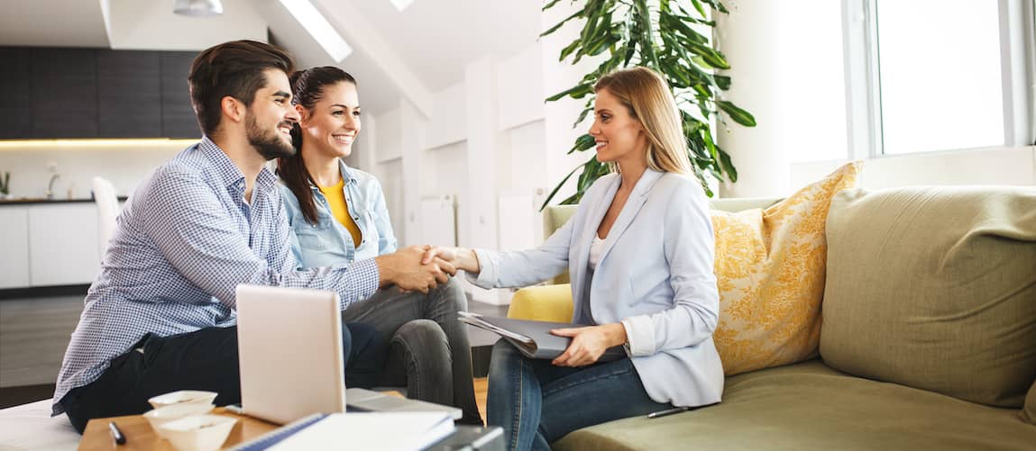 Stock photo showing an agent shaking hands with a couple, representing a real estate transaction or agreement.