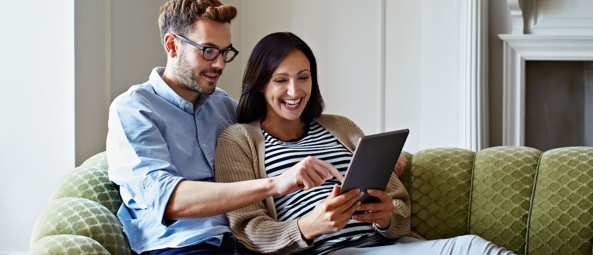Couple sitting on a couch, having a conversation or relaxing together while looking at something on the tablet.