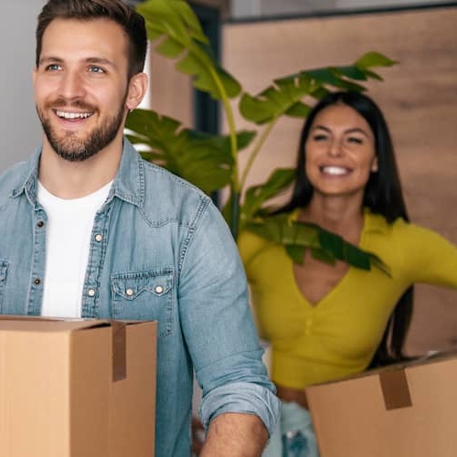 Young couple moving boxes and a houseplant into new home.