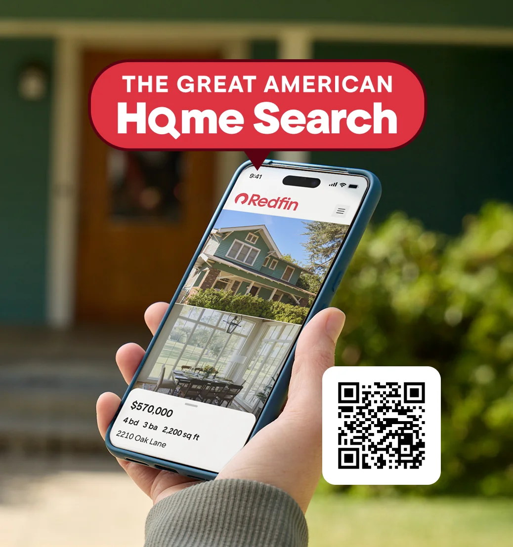 Image of a hand holding a phone in front of a green house.