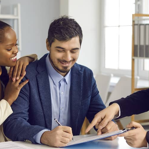 Couple signing documents and smiling, indicating a positive real estate transaction.