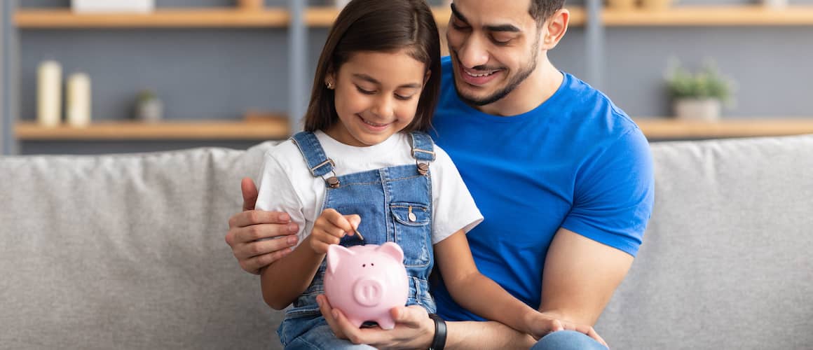 Little girl and dad saving money in piggy bank