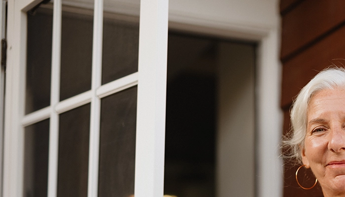 Woman with large gold hoop earrings smiling and holding front door.