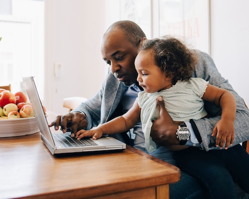 Father sitting at a table with his daughter while he shows her the laptop.