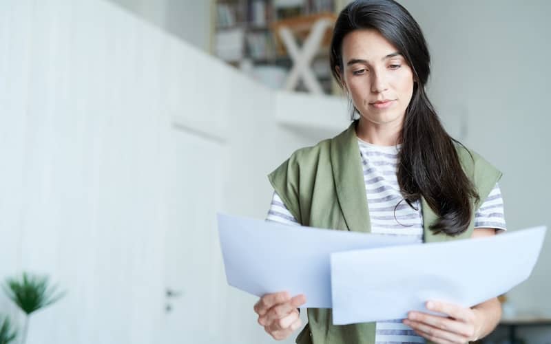 Woman holding two pieces of paper and contemplating them.