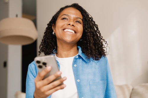 Young woman in apartment, smiling and holding phone.