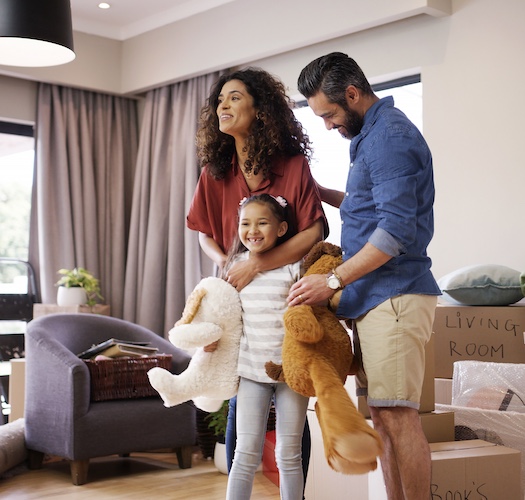 Couple with daughter smiling among boxes inside newly moved into home.