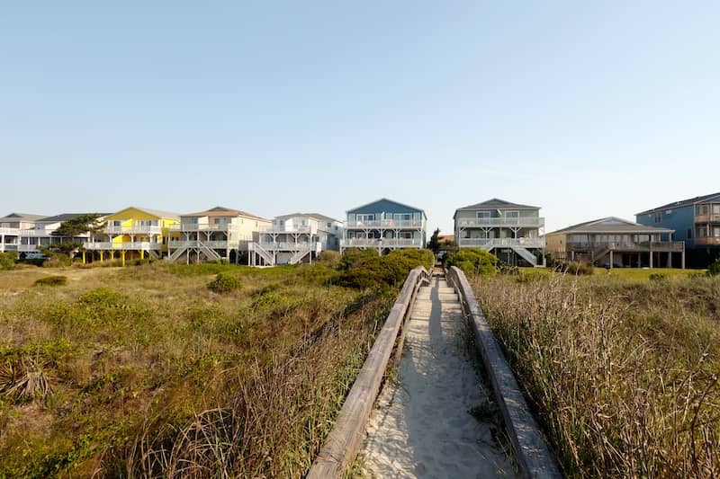 Beachfront walkway leading up to tall houses on the shoreline.