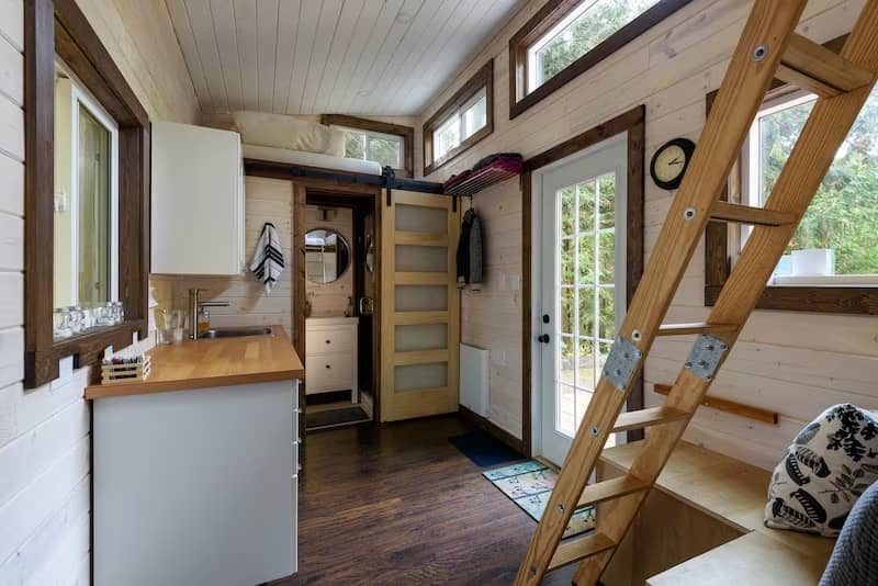 Interior of tiny home with loft, wood trimmed windows, plenty of light from windows throughout and white shiplap walls.