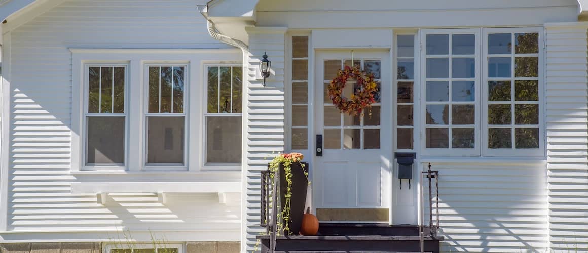 Front view of white bungalow with autumn wreath and pumpkin on top step.