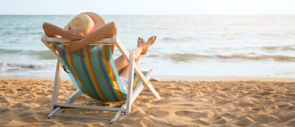 Woman wearing a sun hat and laying back in a chair on the beach.