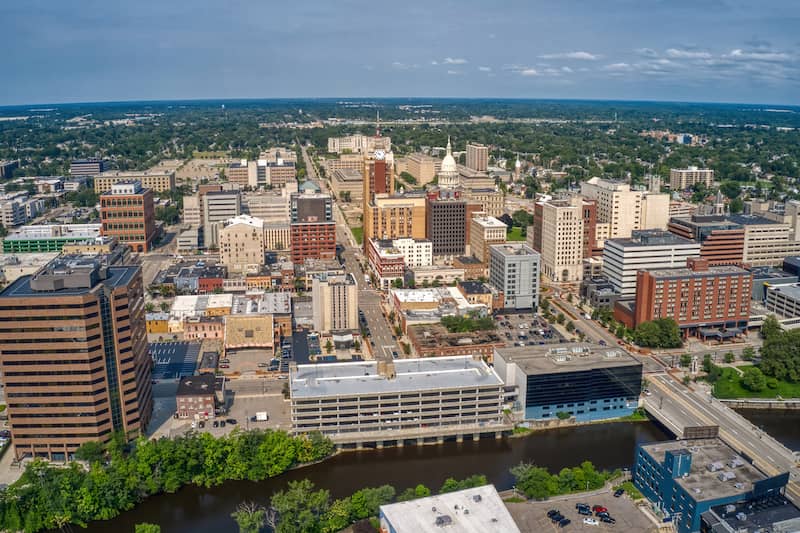 RHB Assets From IGX: Aerial view of Lansing, Michigan's downtown area, showcasing the Capitol building, river, and urban landscape.