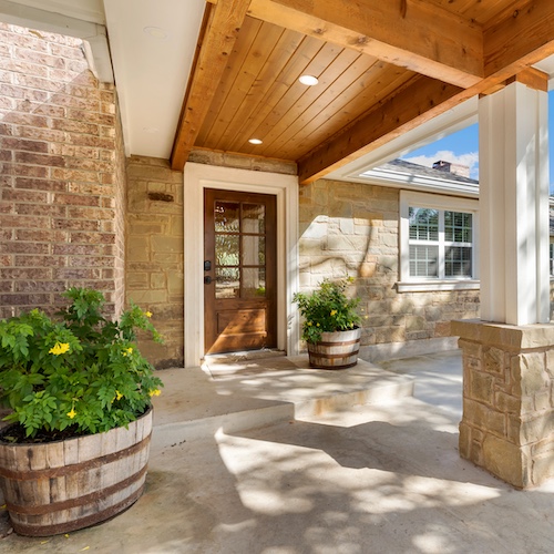 Front porch of an Arkansas house with plants in rustic barrels.