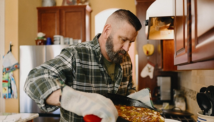 Man pouring food into a crock pot from a cast iron pan.