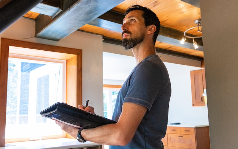 Man appraising house and carrying portfolio while taking notes.