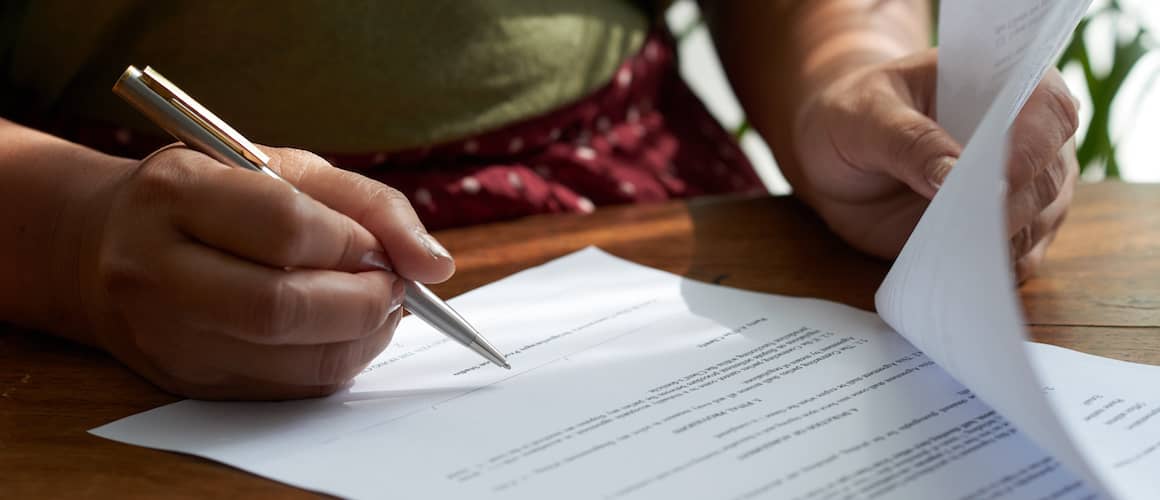 RHB Assets From IGX: Woman signing papers at a table with a real estate agent in a professional office.