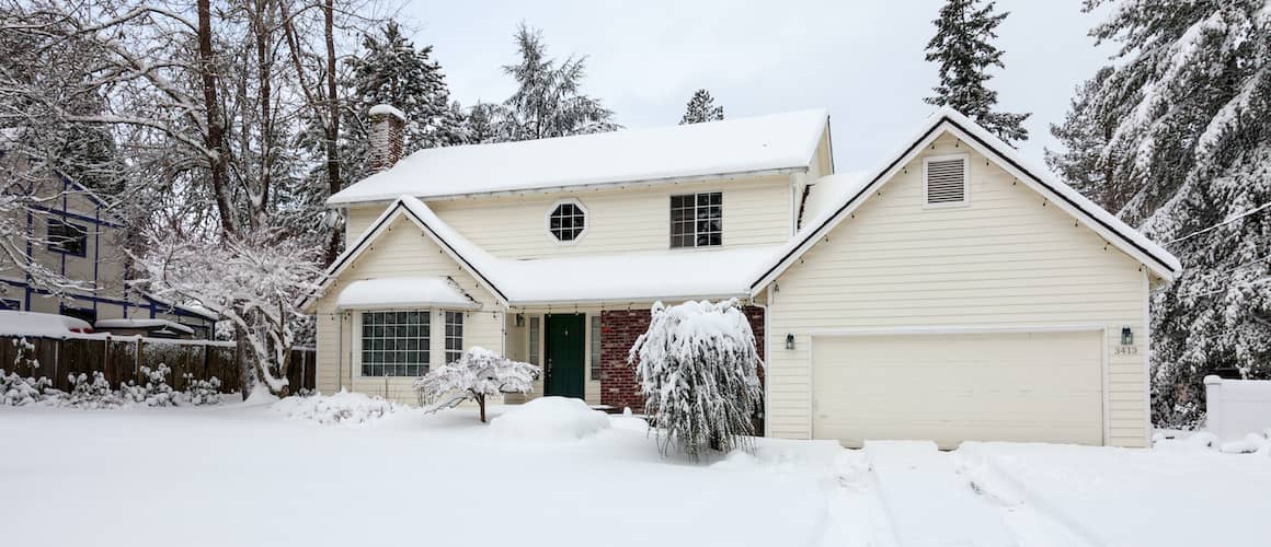 Two-story white house in winter with snowy lawn and trees.