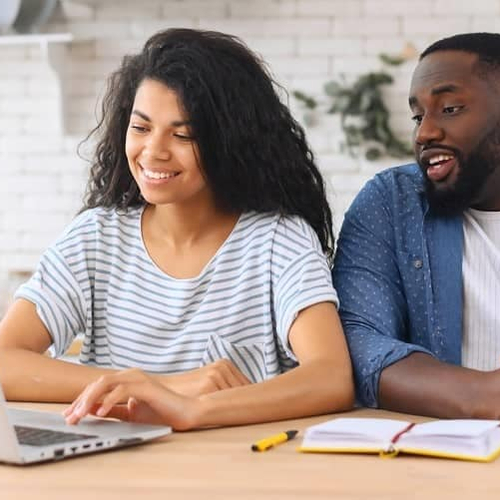 A couple looking at a computer in a kitchen setting.