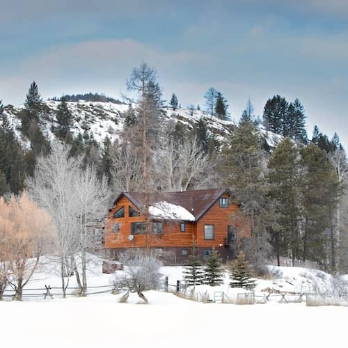 Natural wood sided home surrounded by large trees on a clear, winter day.