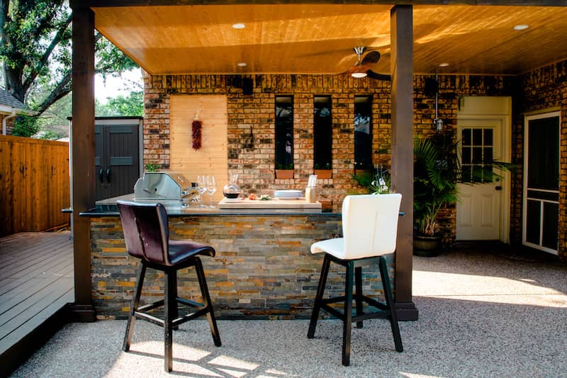 RHB Assets From IGX: A small backyard featuring an outdoor kitchen with a built-in grill and countertop.