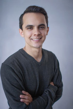 Headshot of a man standing in front of a blue background, smiling with his arms crossed.