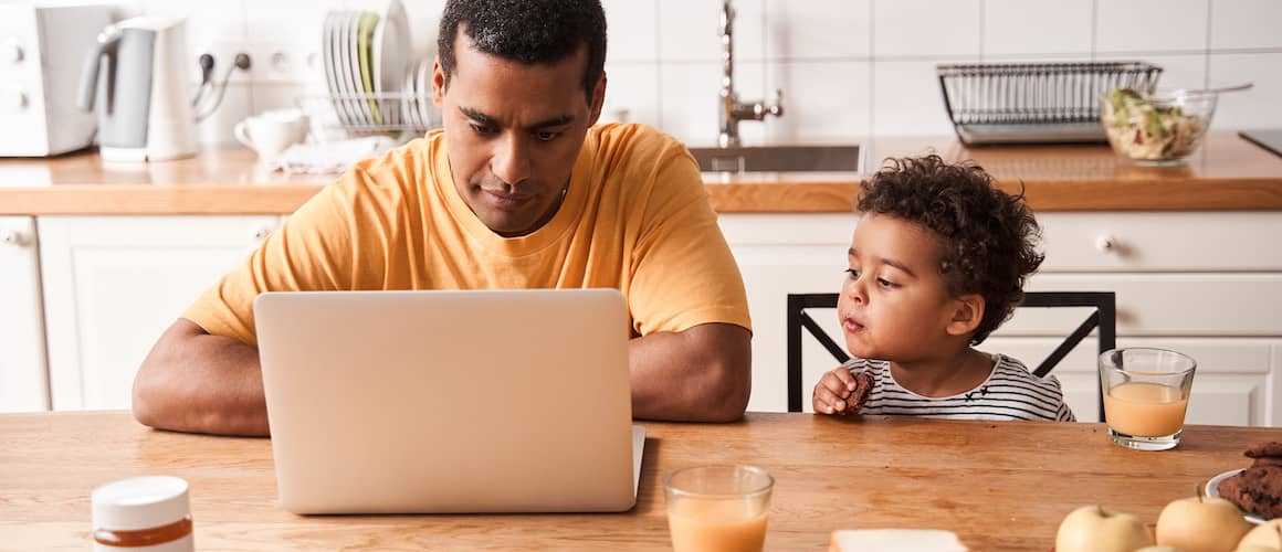 A man working in his kitchen while his child sitting beside is looking at it.