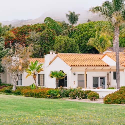 White ranch style home with tiled roof in California surrounded by trees.