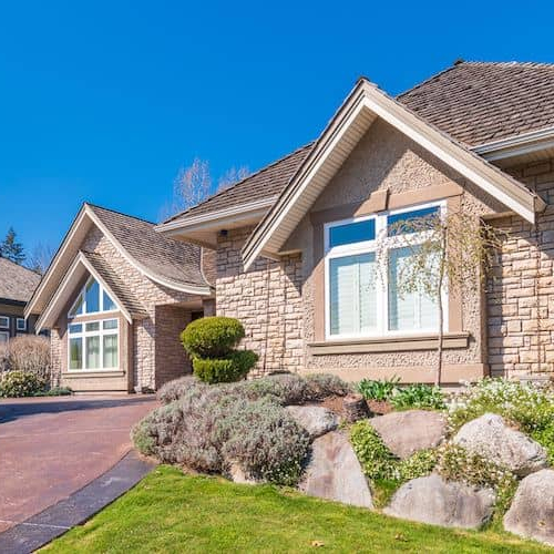 An elegant home featuring a driveway and meticulously designed landscaping.