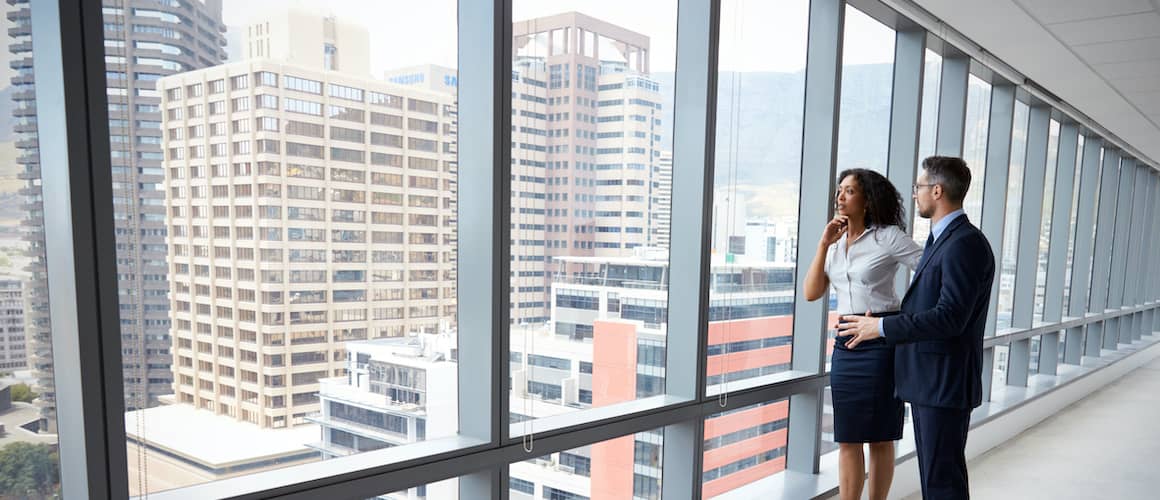 Possibly two real estate agents talking about something with a view of commercial real estate buildings from the window.