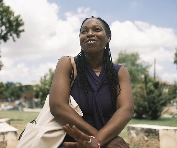 A smiling woman with a shopping bag sits outside.