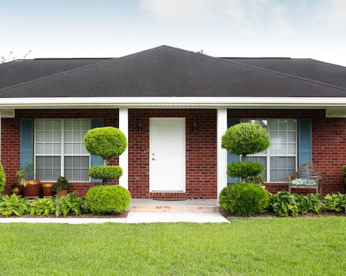 A single storey red brick house with a green front yard.